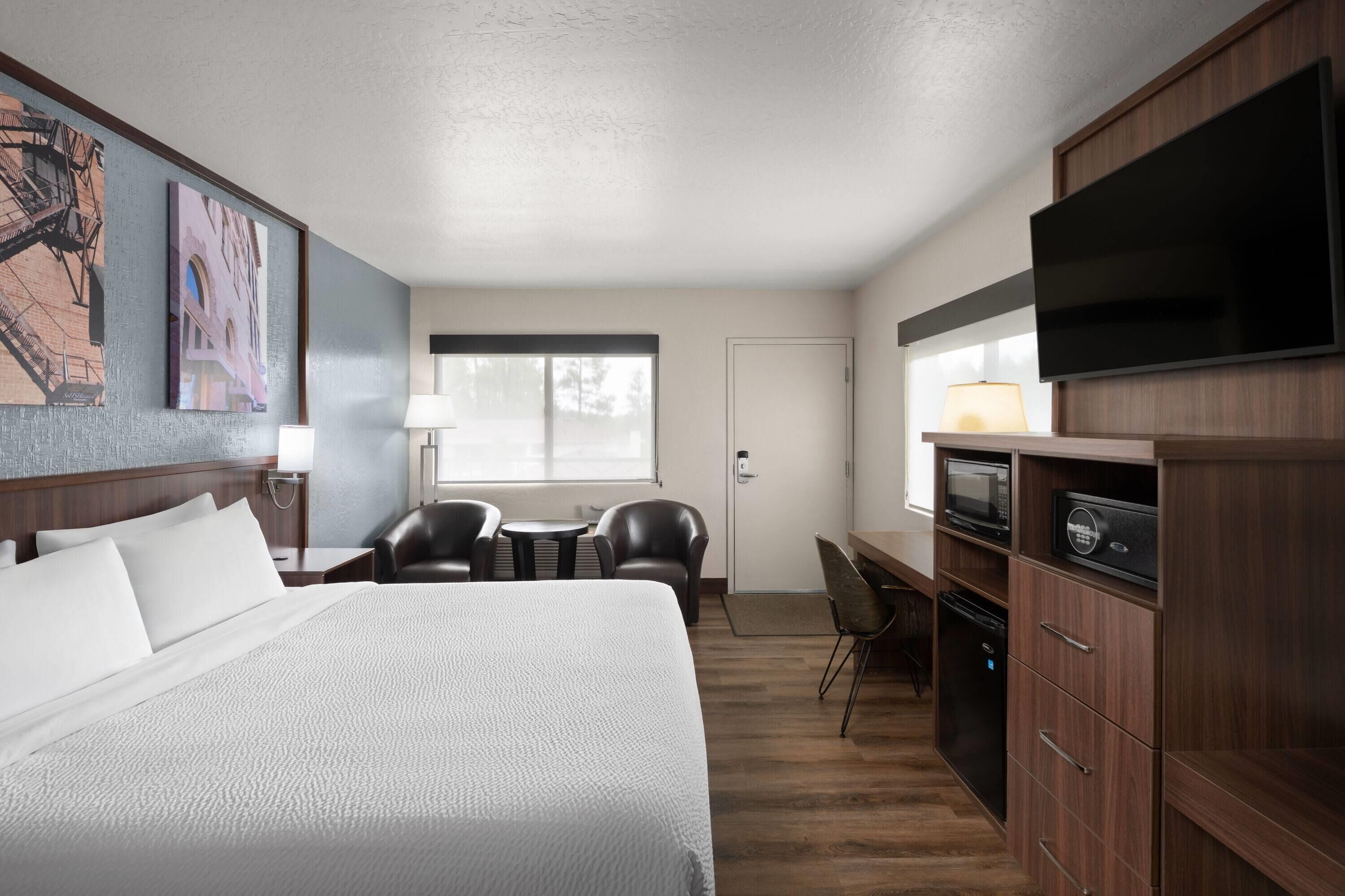A hotel room with a large bed, a desk with a chair, a television, and a microwave.