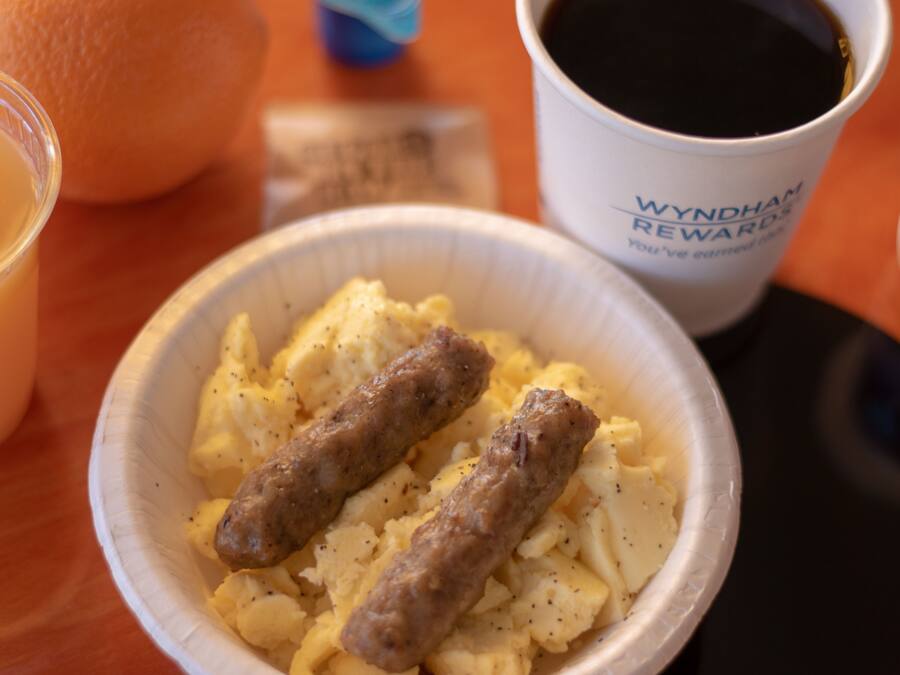 A bowl of scrambled eggs with sausages, a cup of coffee, and a container of yogurt.