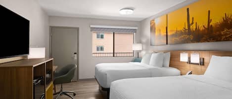 A hotel room with two beds, a TV, a desk, and a painting of a desert landscape.