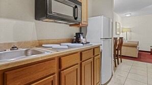 A compact kitchen with wooden cabinets, a stainless steel sink, a microwave, and a refrigerator. - Marina Inn & Suites Chalmette - New Orleans (Chalmette)