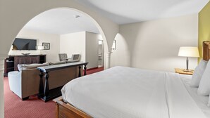 A hotel room with a large bed, a desk with a chair, a television, and a small table with a lamp. - Marina Inn & Suites Chalmette - New Orleans (Chalmette)