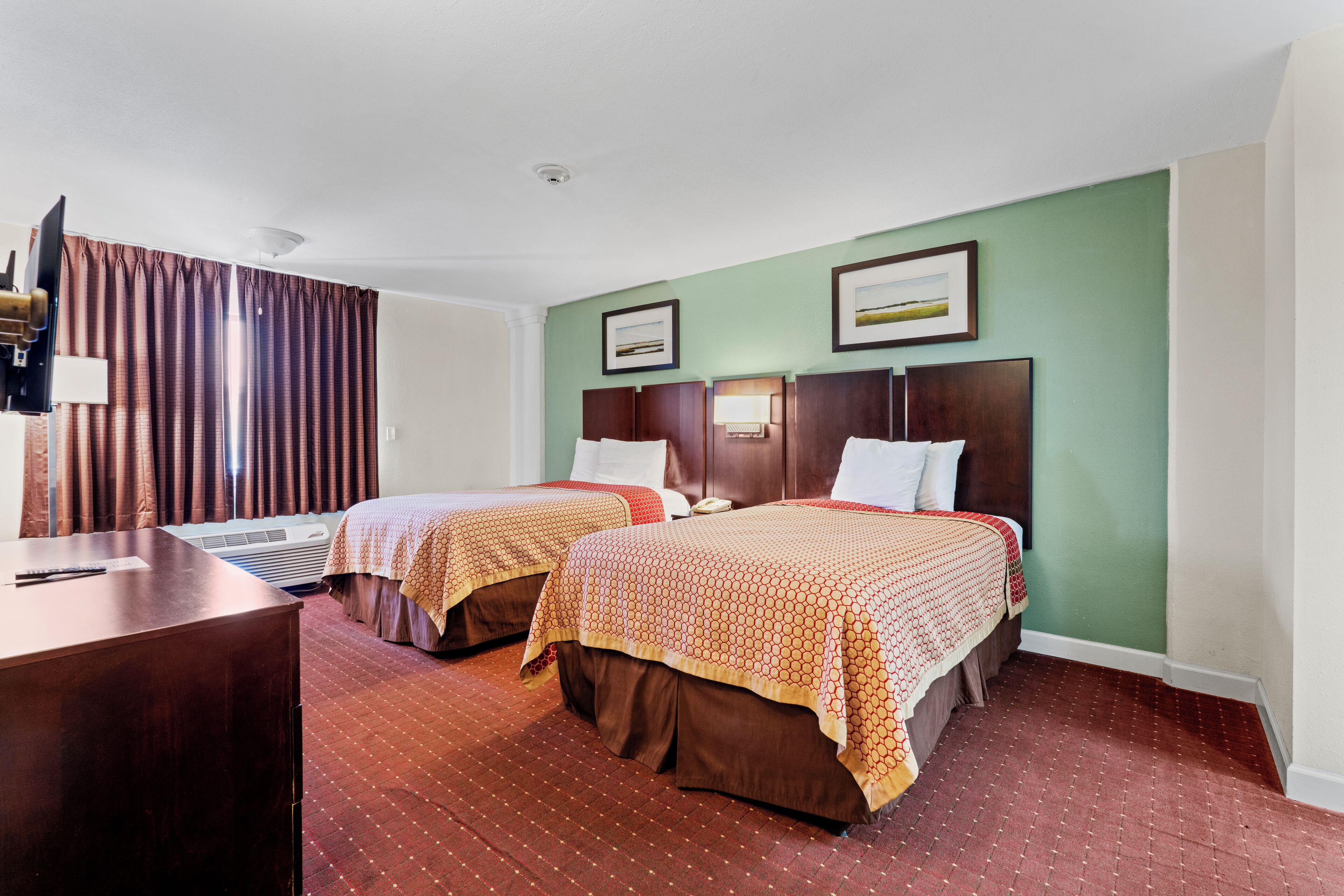 A hotel room with two beds, a desk, and an air conditioning unit.