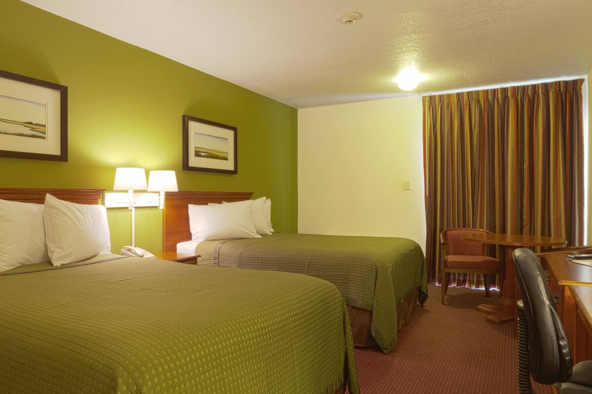 Une chambre d’hôtel avec deux lits, un bureau avec une chaise et une fenêtre avec des rideaux.