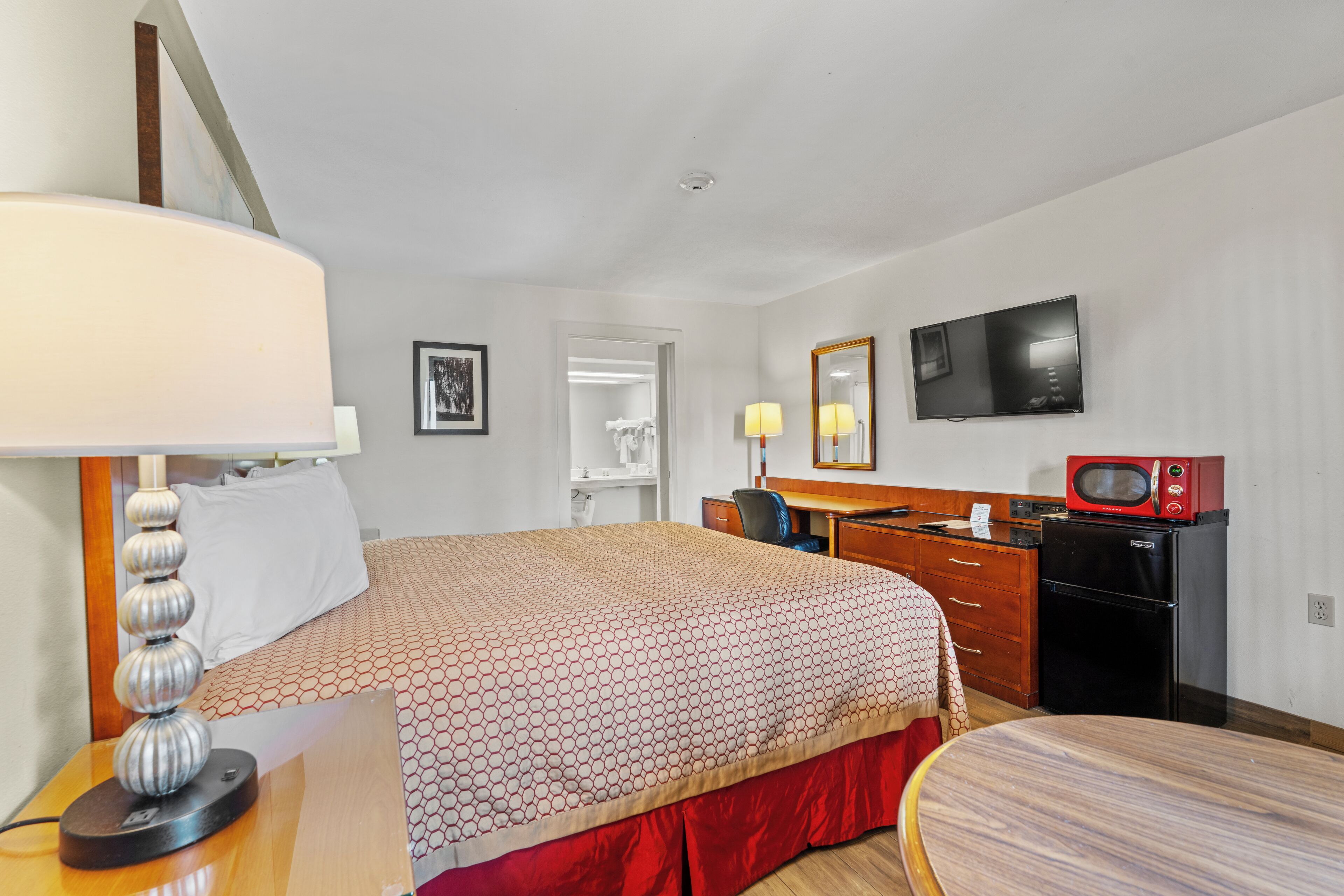 A hotel room with a bed, desk, chair, TV, microwave, and a mirror.