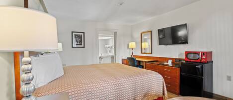 A hotel room with a bed, desk, chair, TV, microwave, and a mirror.