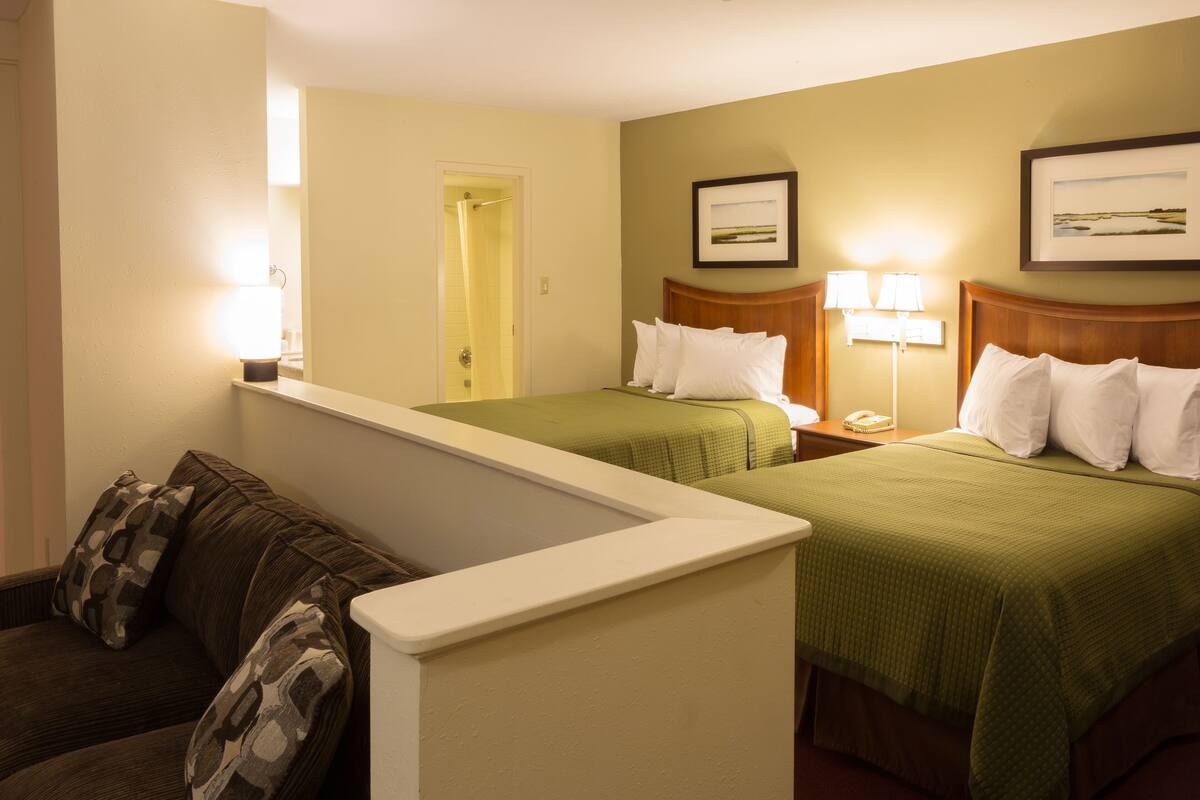 Une chambre d’hôtel avec deux lits, un canapé, un miroir et une porte donnant sur une salle de bain.