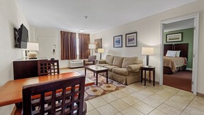 A hotel room with a dining area, a sofa, a bed, and a television. - Marina Inn & Suites Chalmette - New Orleans (Chalmette)