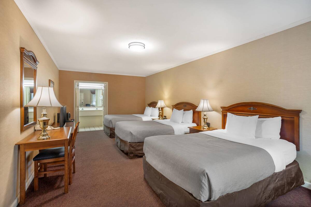 A hotel room with two beds, a desk with a chair, a mirror, and a window.