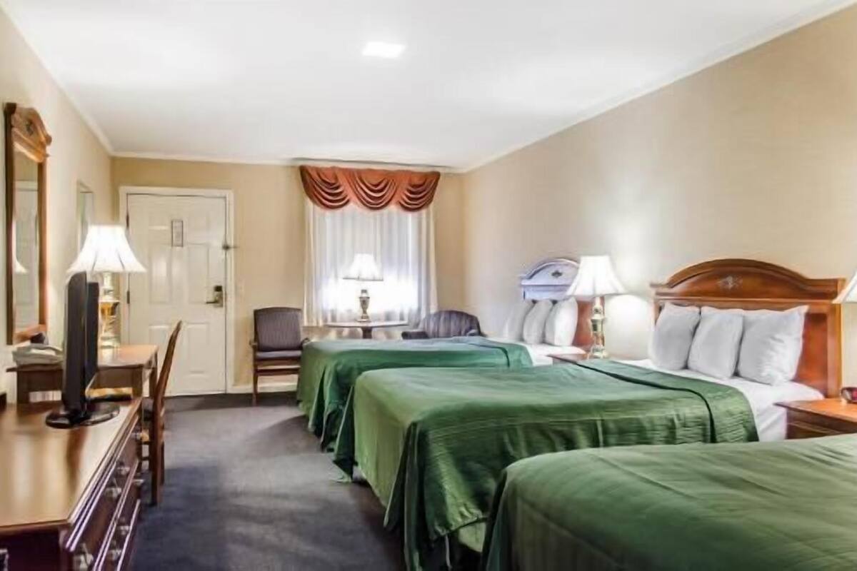 A hotel room with two beds, a desk, a chair, and a lamp.