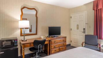 A hotel room with a bed, a desk with a computer, a microwave, a telephone, a chair, and a door.