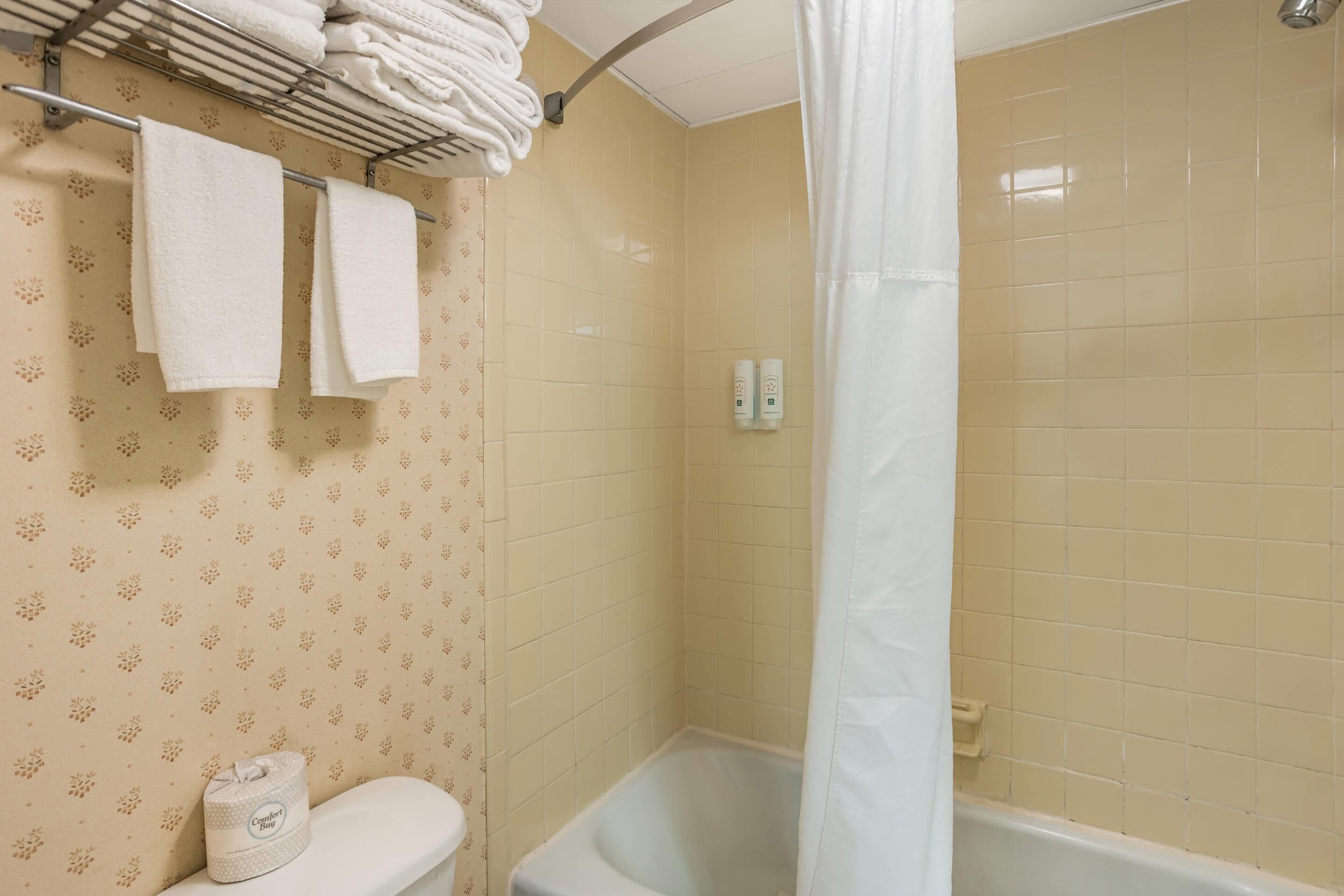 A bathroom with a bathtub, a toilet, and a towel rack with folded towels.