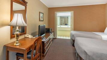 Habitación de hotel con un escritorio de madera, una lámpara, un televisor, un teléfono, una cama y una ventana con vistas al exterior.