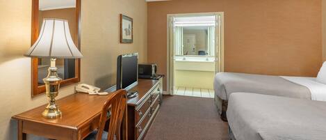A hotel room with a wooden desk, a lamp, a television, a telephone, a bed, and a window with a view of the outside.