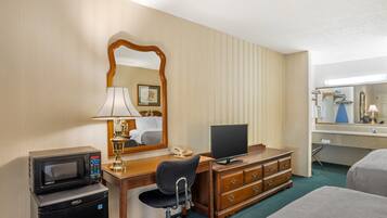 A hotel room with a desk, a chair, a dresser, a bed, a microwave, a telephone, and a television.