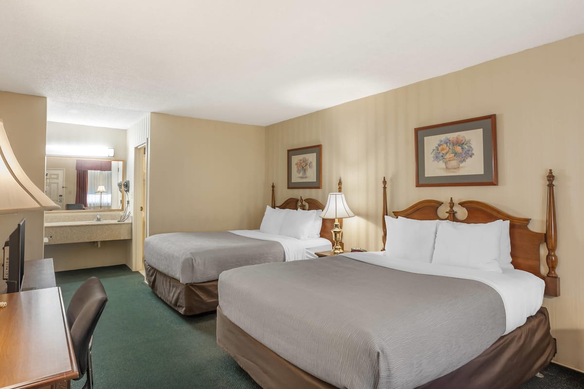 A hotel room with two beds, a desk, a chair, a mirror, and two framed pictures on the wall.