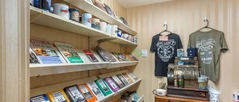 Una habitación con estanterías llenas de libros, un mueble de madera con diversos objetos, y dos camisetas colgadas en la pared.