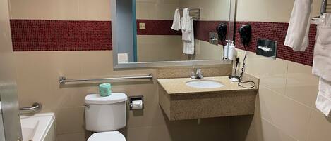 Ein Badezimmer mit Toilette, Waschbecken, Spiegel, Handtuchhalter und einem Händetrockner.