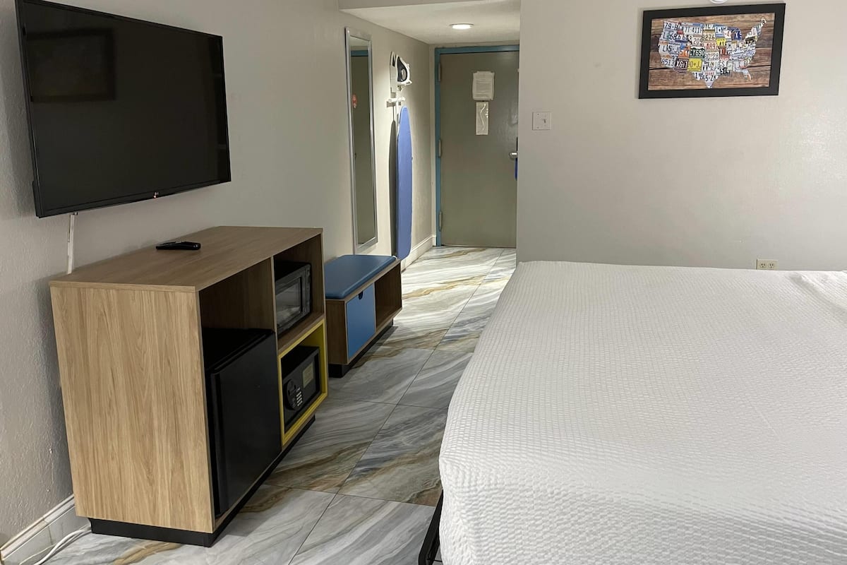 Ein Hotelzimmer mit einem Bett, einem an der Wand befestigten Fernseher, einem Schreibtisch mit Stuhl und einer Tür zu einem Badezimmer.