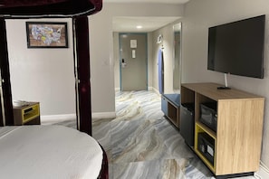 Ein Hotelzimmer mit Bett, Fernseher, Mikrowelle und einem durchgegangenen Türspalte sichtbaren Badezimmer.