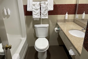 A bathroom with a toilet, a sink, and a bathtub. There are towels hanging on a rack and toiletries on the wall. - Days Inn by Wyndham Jersey City / NYC Area (Jersey City)