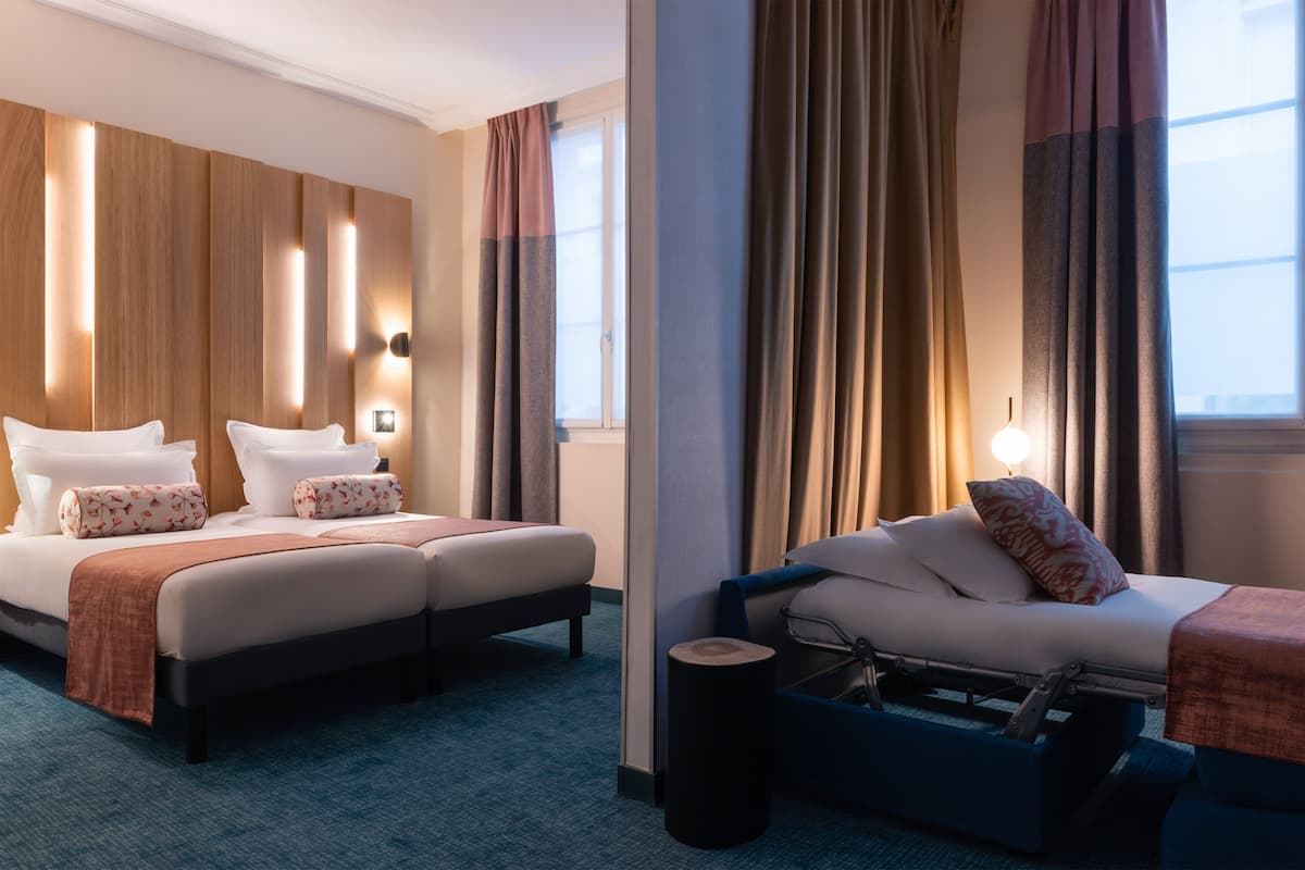 A hotel room with two beds, a sofa, a small table, and a window with curtains.