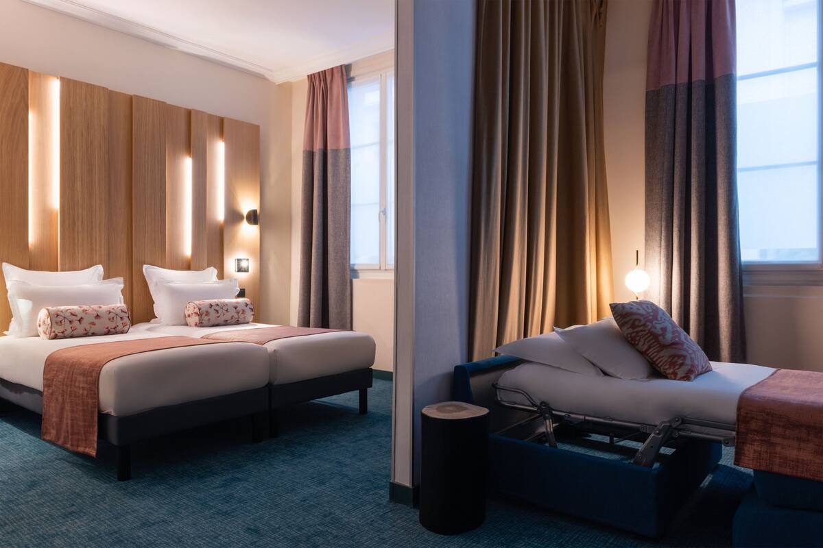 Hotellihuone, jossa on kaksi sänkyä, sohva, pieni pöytä ja ikkuna, jossa on verhot.