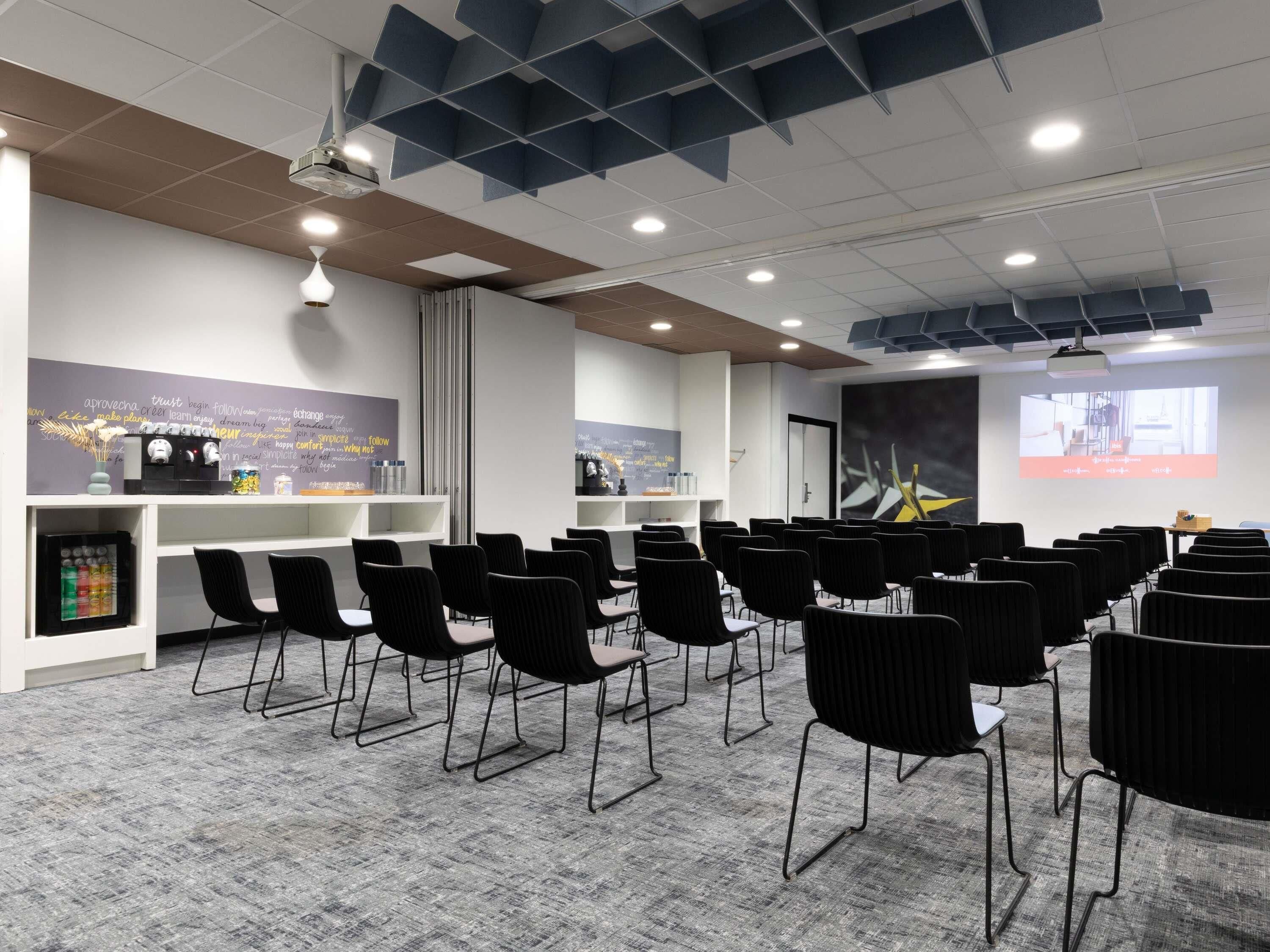 A conference room with rows of chairs, a projector screen, and a whiteboard with motivational quotes.