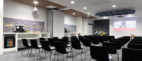 A conference room with rows of chairs, a projector screen, and a whiteboard with motivational quotes.