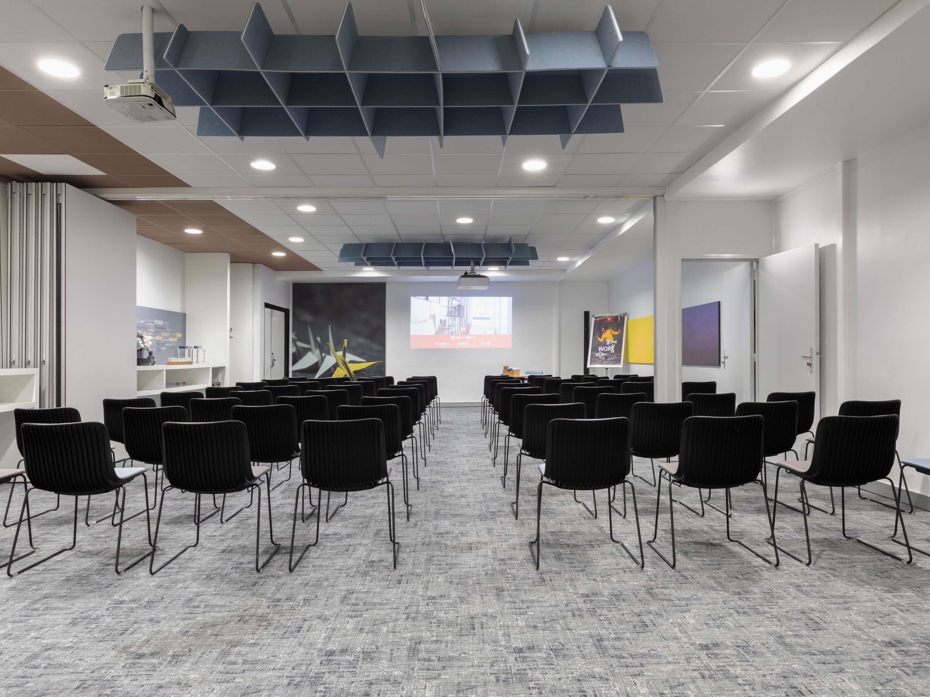 A conference room with rows of chairs, a projector, and presentation screens.