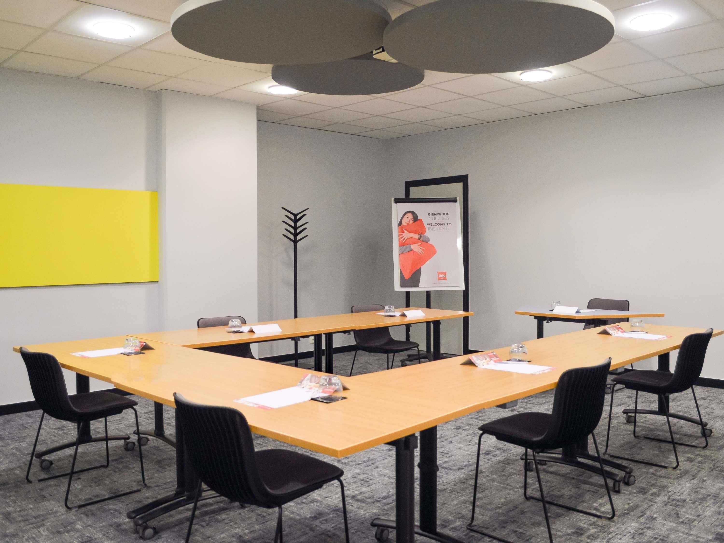 A conference room with long tables, black chairs, and a yellow accent wall.