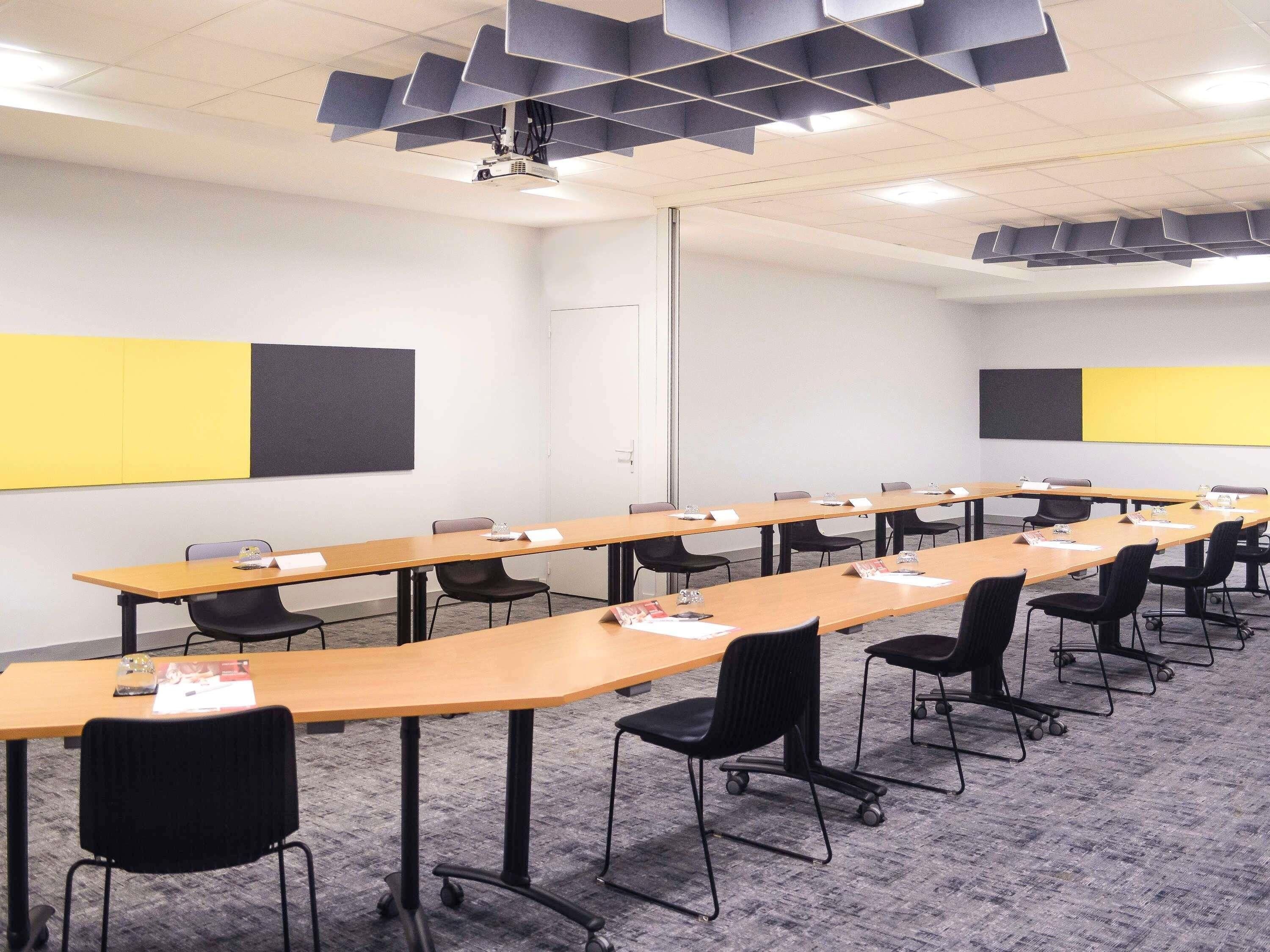A conference room with long tables, black chairs, and a projector on the ceiling.