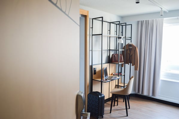 A hotel room with a desk, chair, laptop, and a suitcase.