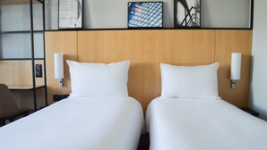 Une chambre d’hôtel avec deux lits simples, une tête de lit en bois et un luminaire fixé au mur.
