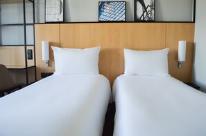 Ein Hotelzimmer mit zwei Einzelbetten, einem hölzernen Kopfteil und einer wandmontierten Lampe.