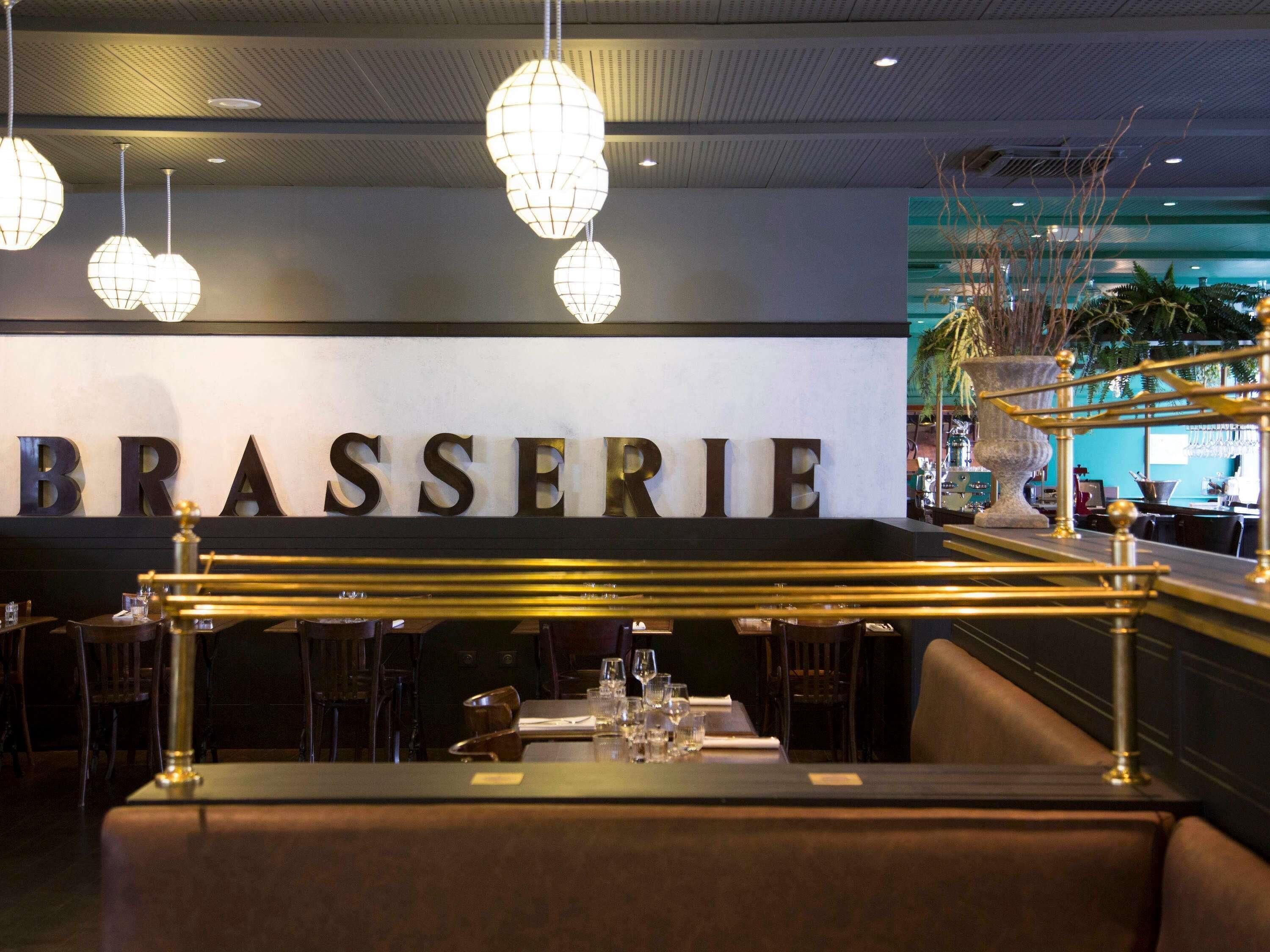 A restaurant interior with a sign reading 'BRASSERIE,' tables set with glasses, and hanging pendant lights.