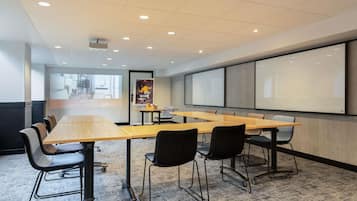 A conference room with a long table, chairs, a projector screen, and a carpeted floor.