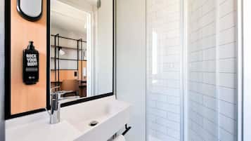 Un baño moderno con un espejo grande, un lavamanos blanco, una toalla y una cabina de ducha de vidrio.