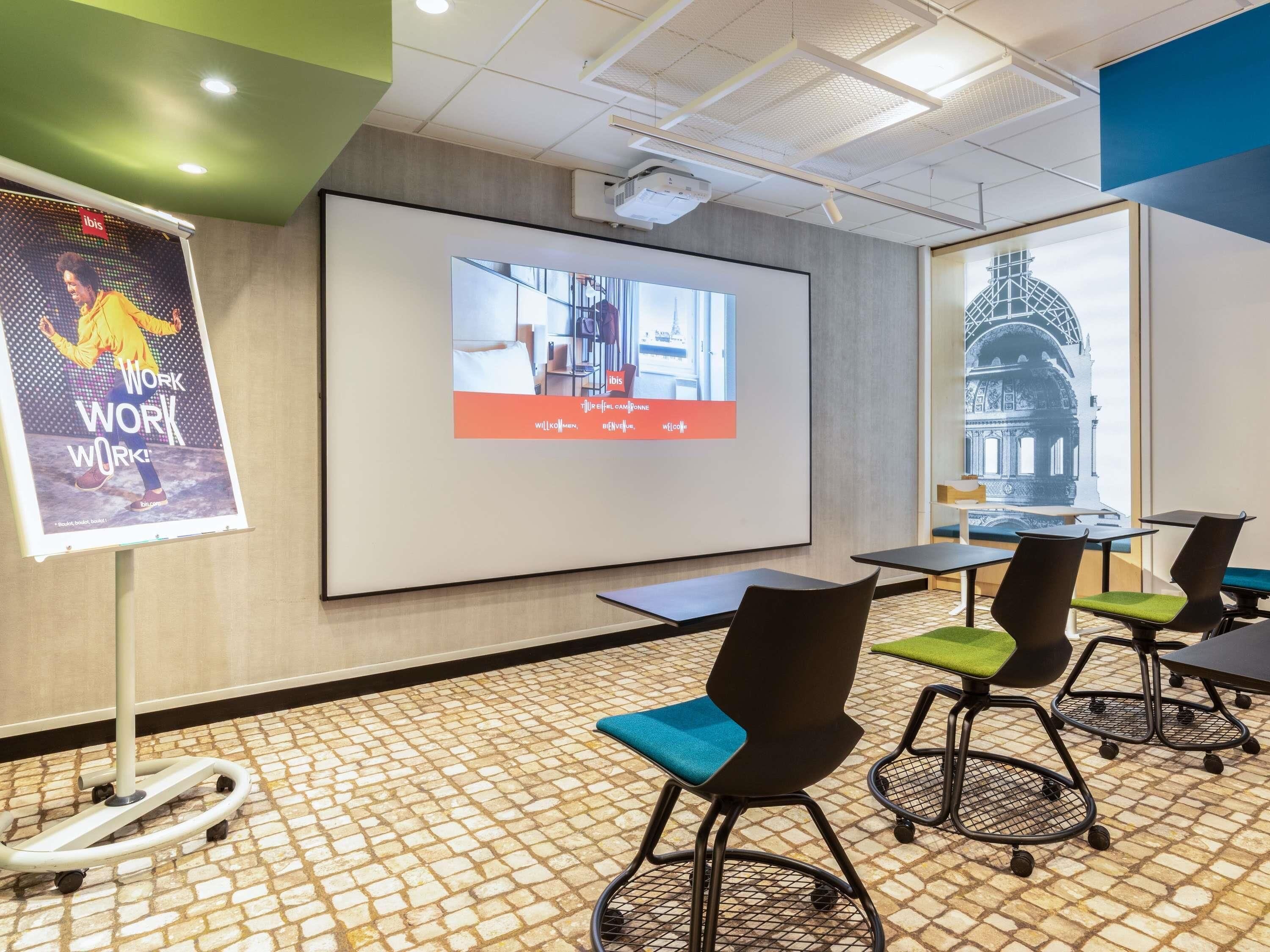 A conference room with a projector screen, a presentation on the wall, and a tiled floor.