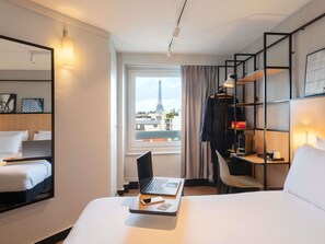 Habitación de hotel con cama, escritorio con computadora portátil, silla, armario y vistas a la Torre Eiffel.