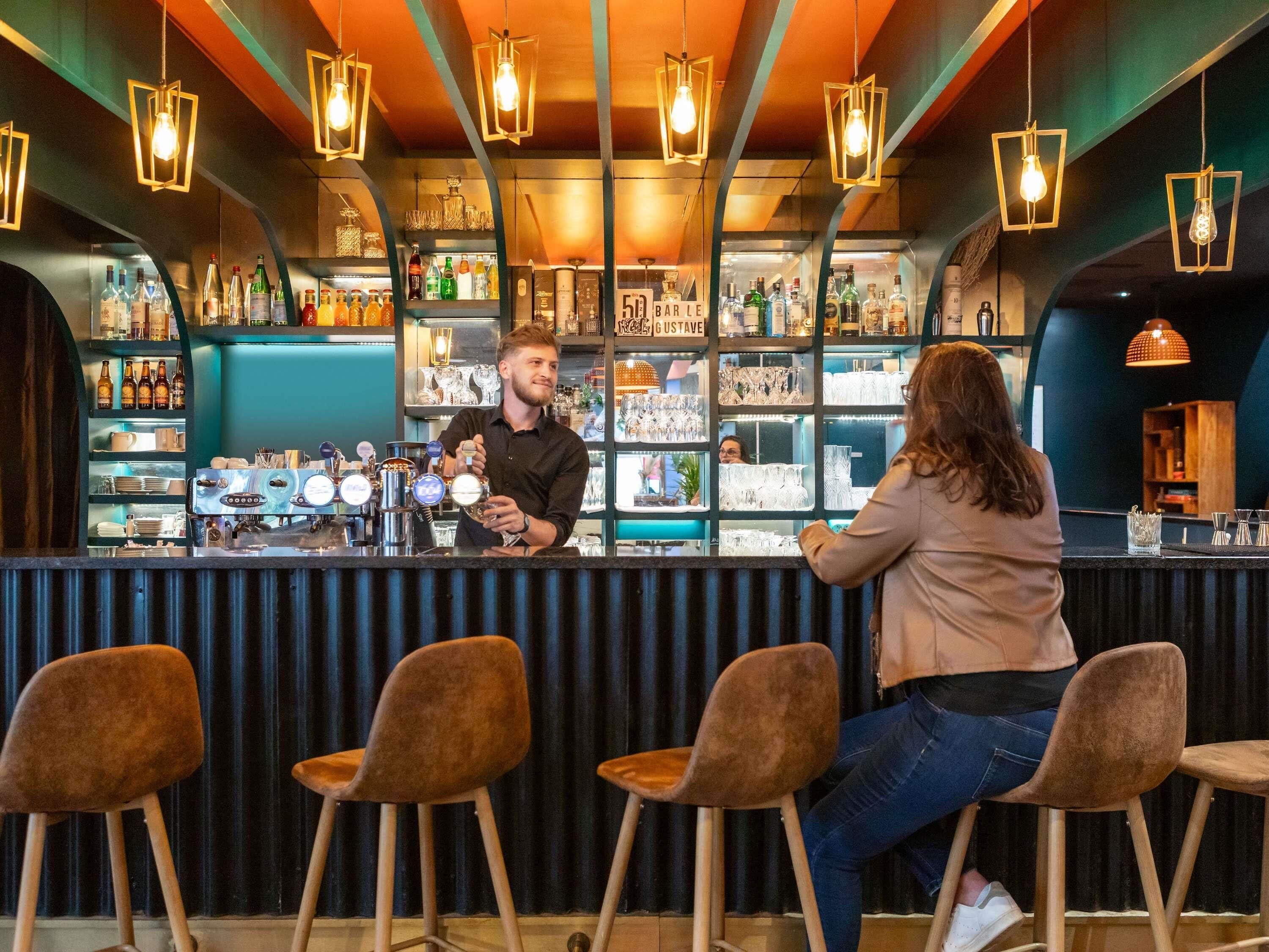 A bar area with a bartender, shelves with bottles, and bar stools.
