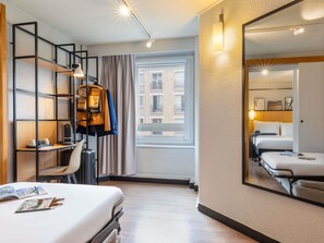 Hotelkamer met een bed, bureau, stoel, kledingkast, spiegel en raam met uitzicht op gebouwen.