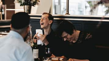 Un comedor con una mesa dispuesta para dos personas, una botella de vino y un jarrón con flores.