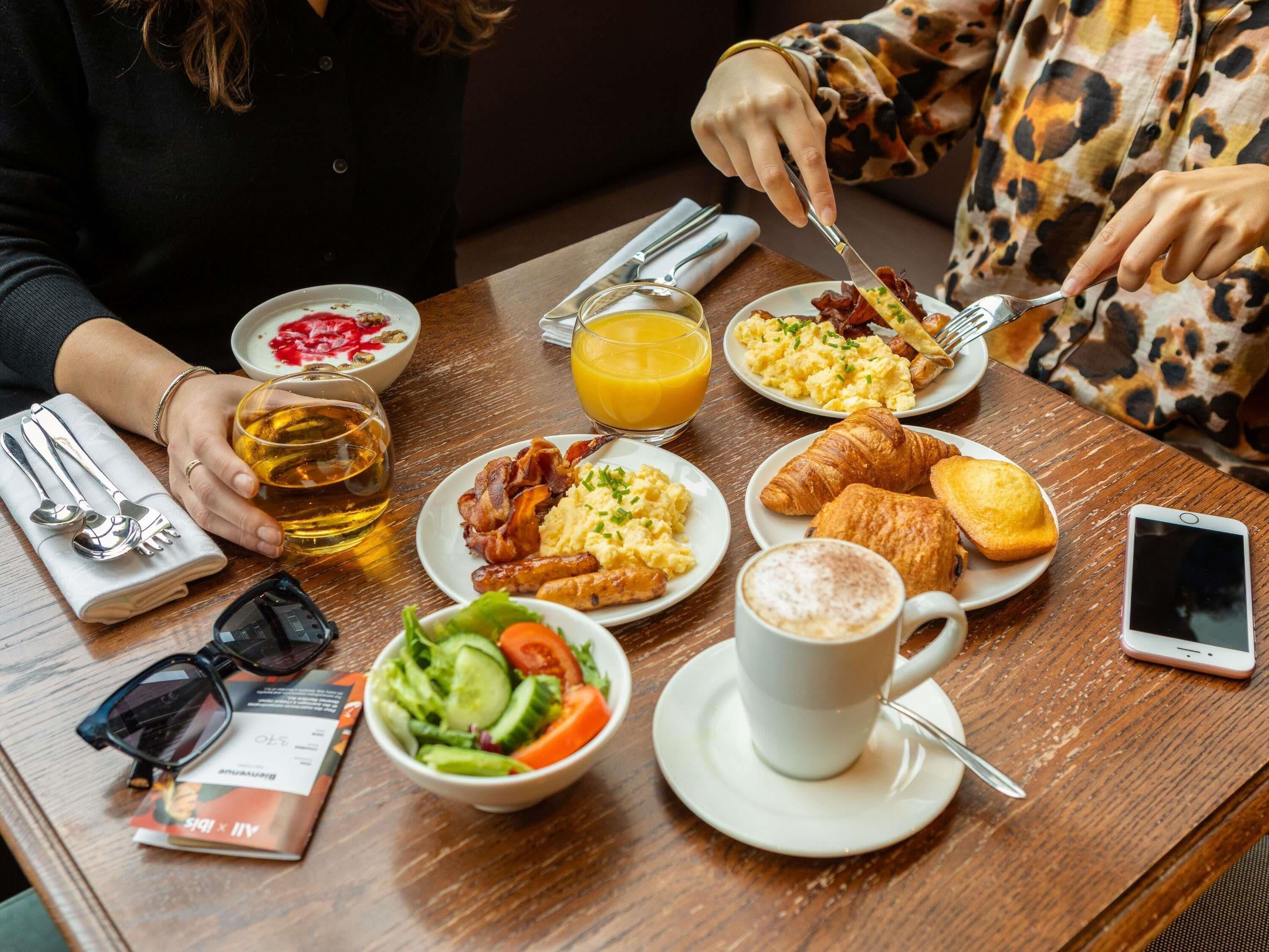 A breakfast table with various food items, a glass of orange juice, a cup of coffee, and a smartphone.