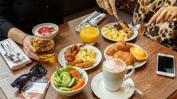 Une table de petit-déjeuner avec divers aliments, un verre de jus d’orange, une tasse de café et un téléphone intelligent.