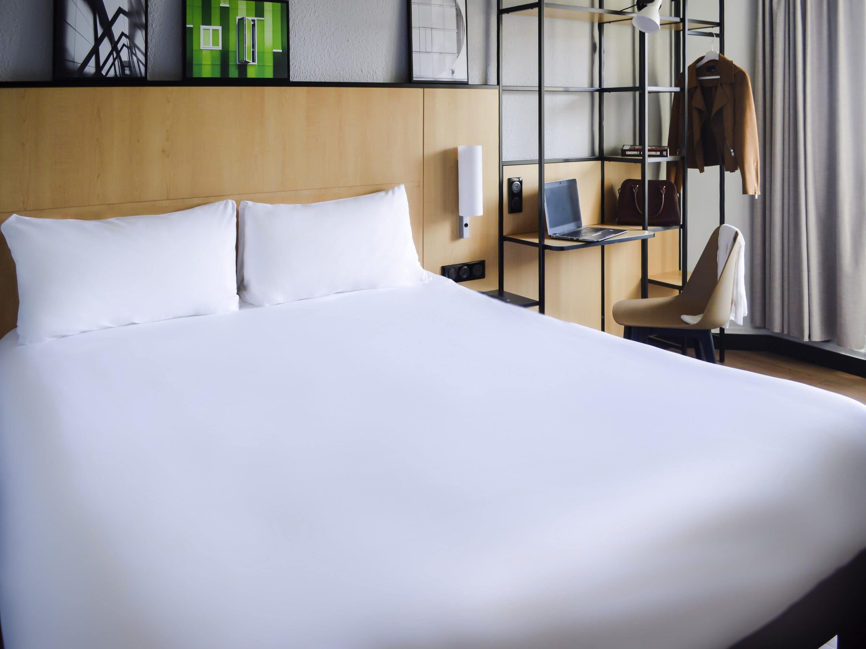 Hotellihuone, jossa on suuri sänky, työpöytä kannettavalla tietokoneella, tuoli ja naulakko.