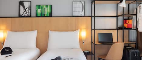 Een hotelkamer met twee bedden, een bureau met een laptop, een stoel, een koffer en een plank met persoonlijke spullen.