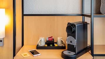 Une machine à café moderne, posée sur une table en bois, avec un smartphone et une barquette de tasses à café.