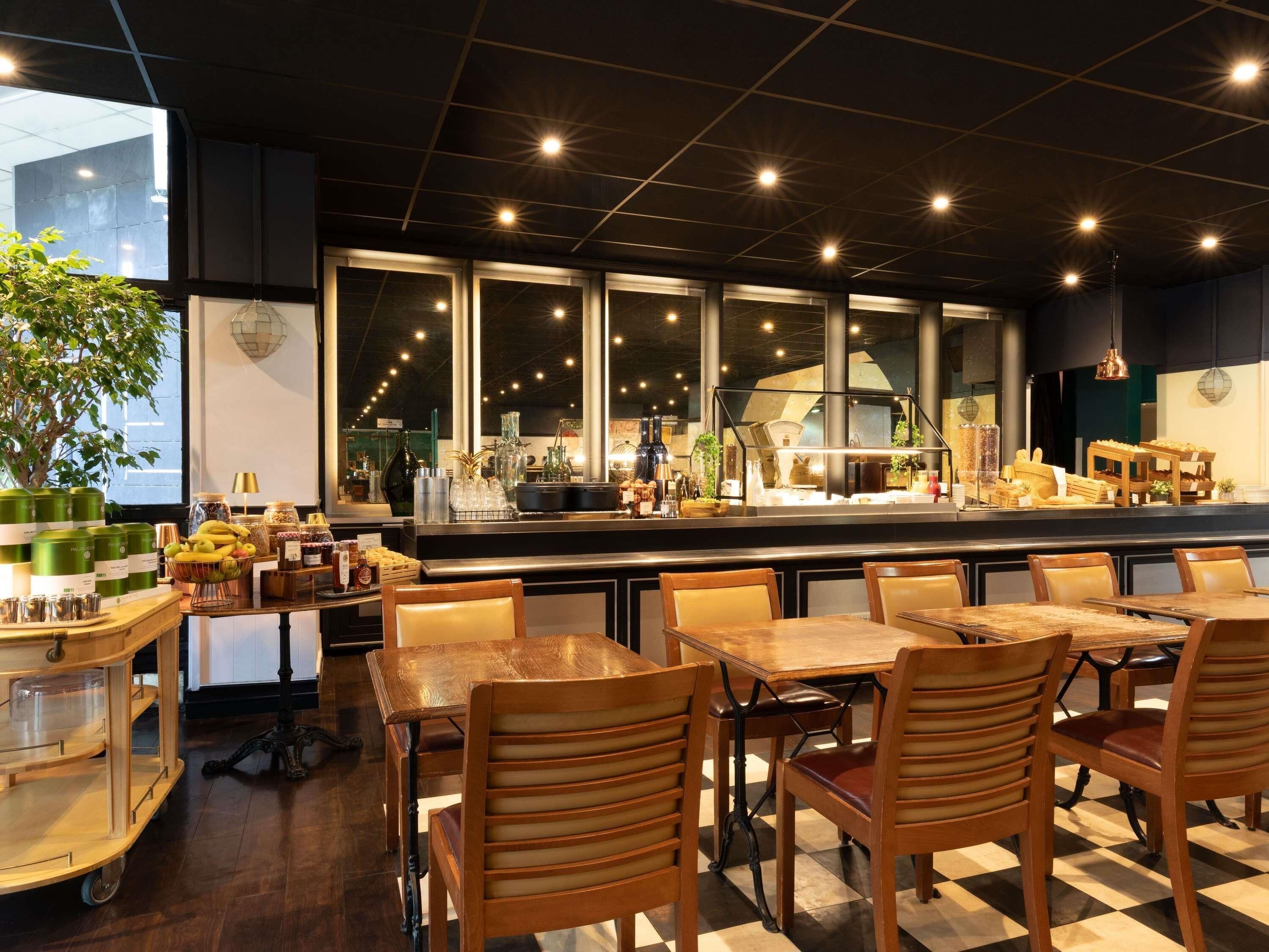 A restaurant interior with a bar area, wooden tables and chairs, and a view through large windows.