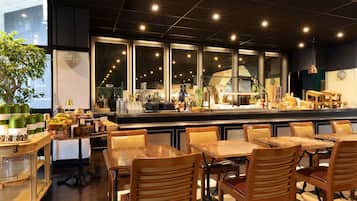 A restaurant interior with a bar area, wooden tables and chairs, and a view through large windows.