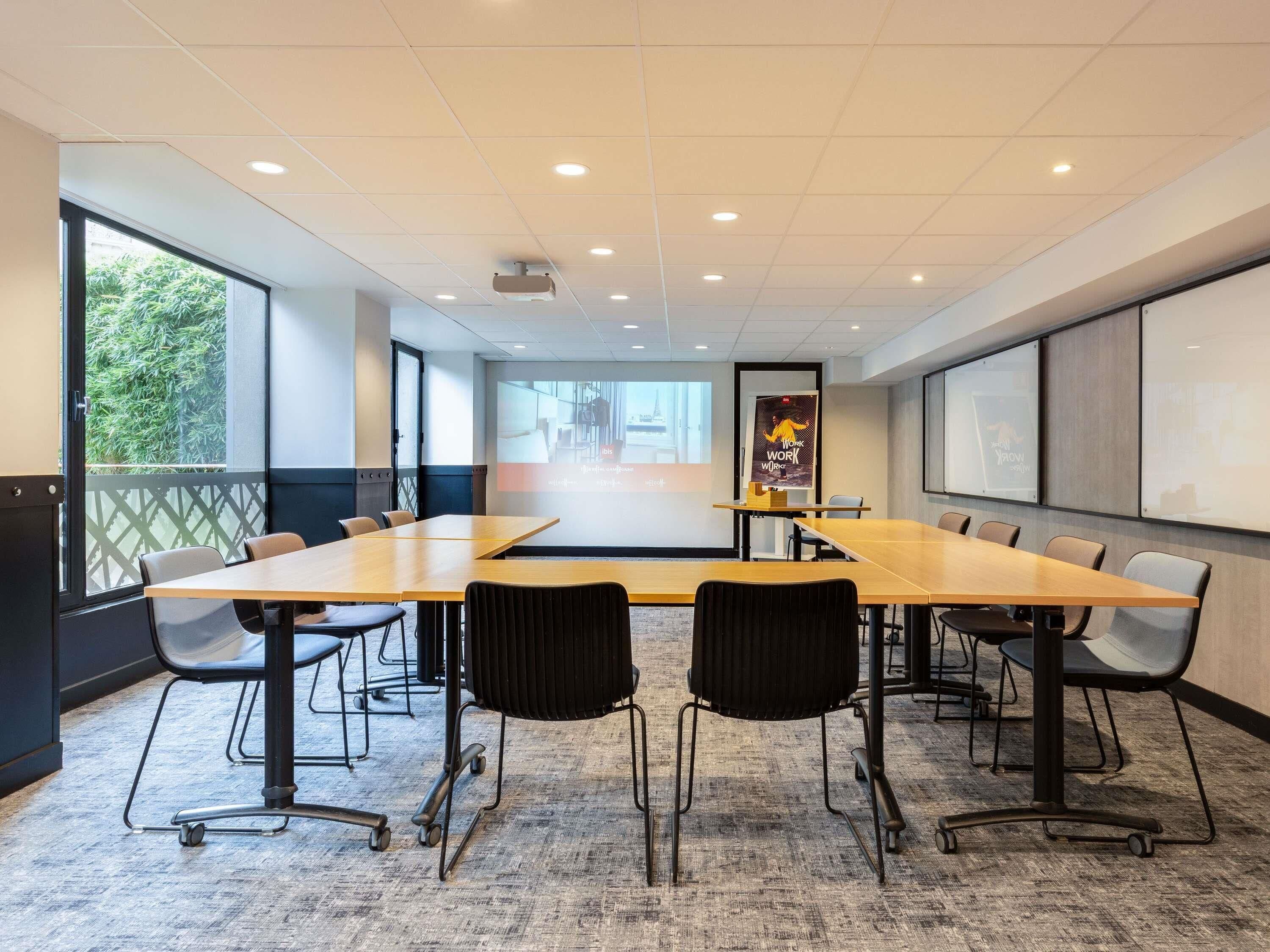 A conference room with a long table, chairs, a projector screen, and a large window.